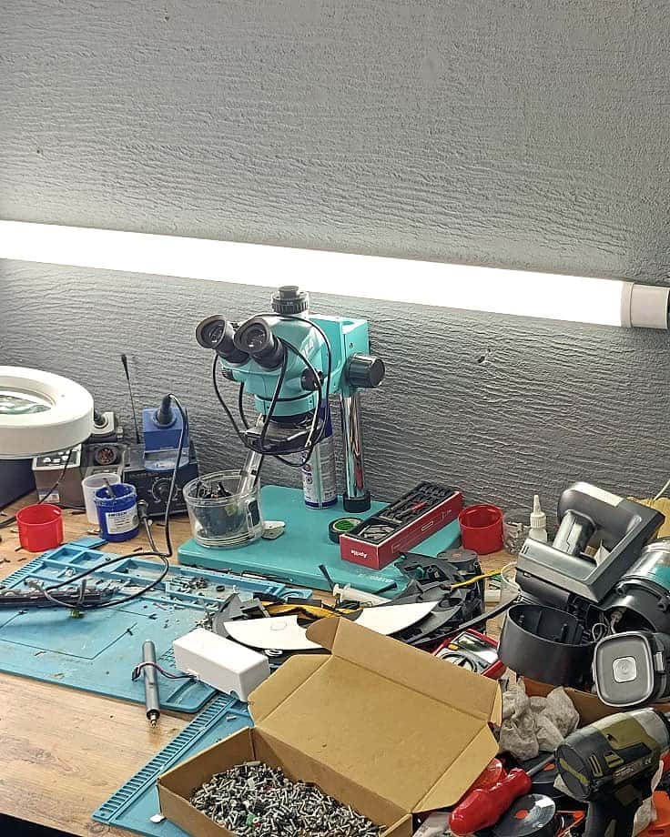 Robotik atölyesinde elektronik kart tamiri tezgâhı: stereo mikroskop, lehim istasyonu ve sökülmüş cihaz parçaları