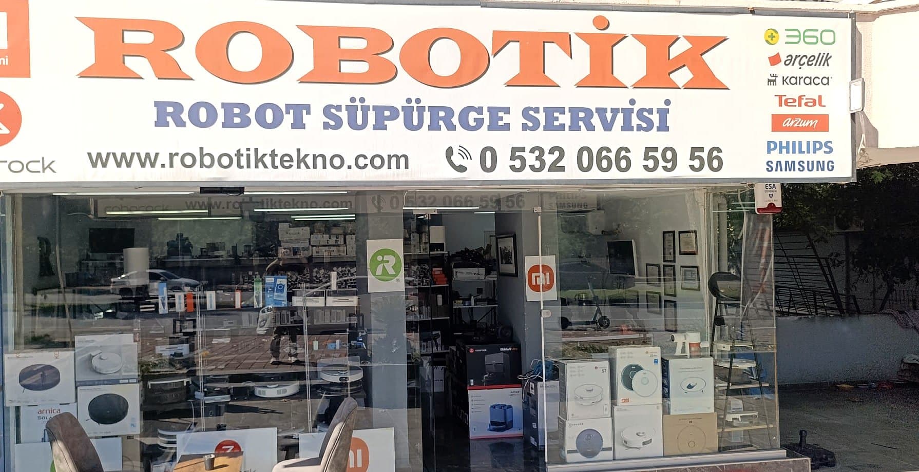 Robotik robot süpürge servisi dükkân cephesi; turuncu ROBOTİK tabelası ve robot süpürge kutularıyla dolu vitrin