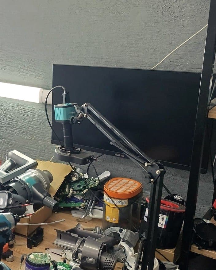 Kart onarım tezgâhında monitöre bağlı kamera mikroskobu; altında incelenen bir devre kartı